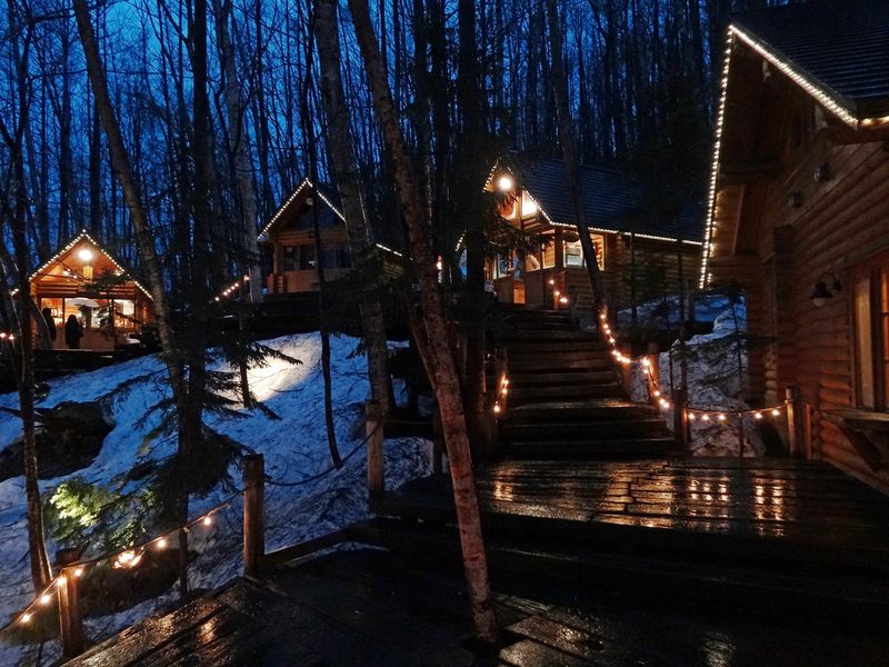 Warm lights illuminating the log cabins and boardwalk at Ningle Terrace during evening